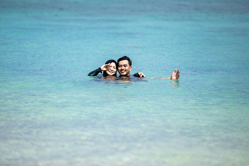 two young asian muslim couple swimming and playing water in the beach of padar island, komodo nasional park