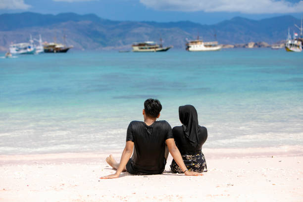 two young asian muslim couple swimming and playing water in the beach two young asian muslim couple swimming and playing water in the beach of padar island, komodo nasional park malay couple full body stock pictures, royalty-free photos & images