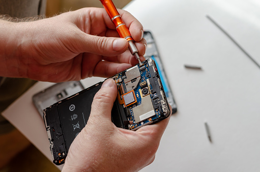 A man is repairing a Smartphone. Hands hold a screwdriver and disconnect the sim card loop. Services Repair. Selective focus.