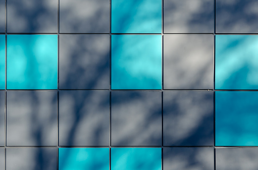 Grey and turquoise alternating squares. Abstract shadows on the exterior wall of the building. The building is clad in multicolored metal sheets. Architecture. Selective focus.