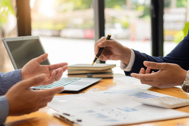 istock Two businessmen with pens pointing to a graph discussing data with modern laptops on a desk. Strategic concepts and close-up business team analysis in the office. 1354117231