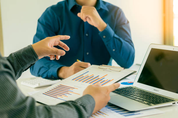 istock Two businessmen with pens pointing to a graph discussing data with modern laptops on a desk. Strategic concepts and close-up business team analysis in the office. 1354117261