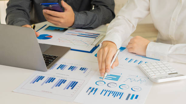 istock Two businessmen with pens pointing to a graph discussing data with modern laptops on a desk. Strategic concepts and close-up business team analysis in the office. 1354117263