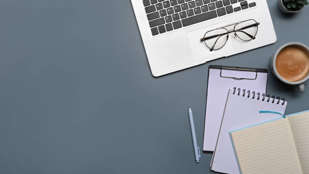 istock Top view clipboard, coffee cup and laptop computer on gray background. 1354139543