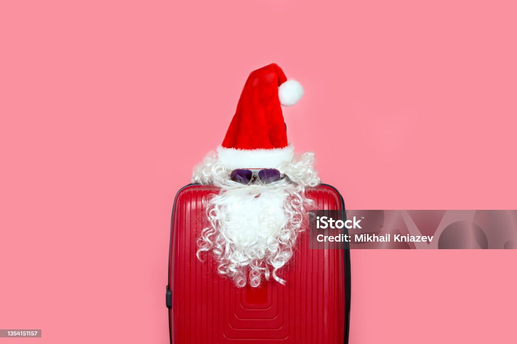 Imitation of Santa Claus from a hat, beard and sunglasses on a suitcase Imitation of Santa Claus from a hat, beard and sunglasses on a suitcase. Use it for tourism and travel in the New Year and Christmas Christmas Stock Photo