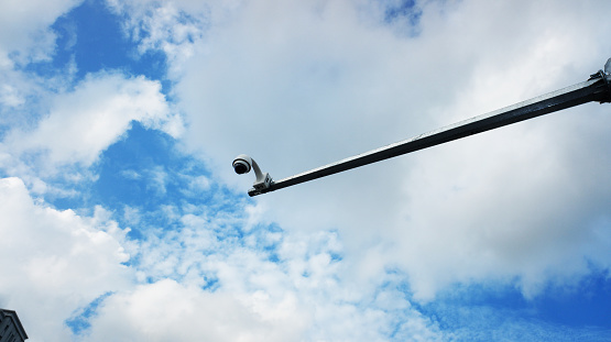 Modern CCTV camera on a lamp post. A blue sky cityscape background. Concept of surveillance and monitoring.