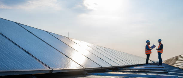 Male engineers discussing while standing on the rooftop of solar plant Male engineers talking with each other while standing on rooftop of solar power plant. two men same clothes stock pictures, royalty-free photos & images