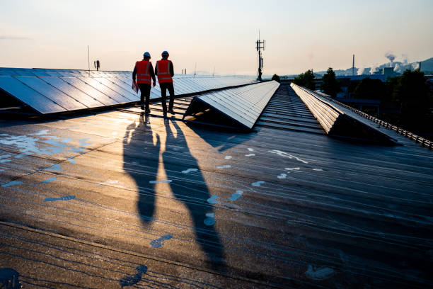 Male engineers walking along rows of photovoltaic panels Rear view of mature male engineers walking along the rows of photovoltaic panels on a rooftop of a solar plant. rooftop solar stock pictures, royalty-free photos & images