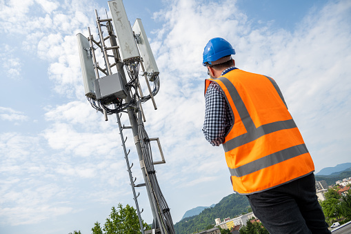 Low angle view of mature male engineer looking at solar powered telecom tower while standing on roof