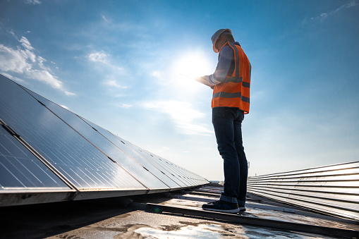 Low angle view of mature male engineer holding plan while working on the rooftop of a solar power plant.