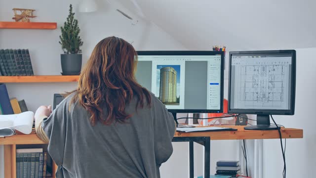 A back view of a woman working with a laptop and two additional monitors on a project of a high-rise building. The concept of working at home using a remote scheme. Quarantine