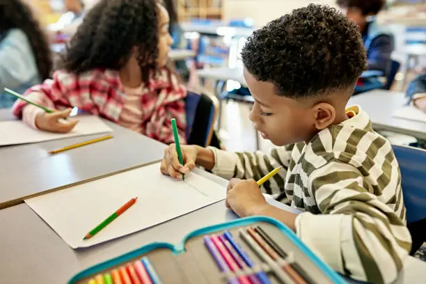 Photo of Focused Schoolboy Drawing Picture with Colored Pencils