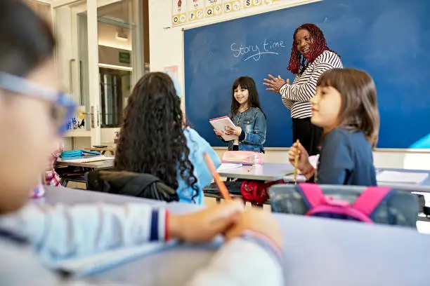 Photo of Young School Girl Reading Story to Classmates