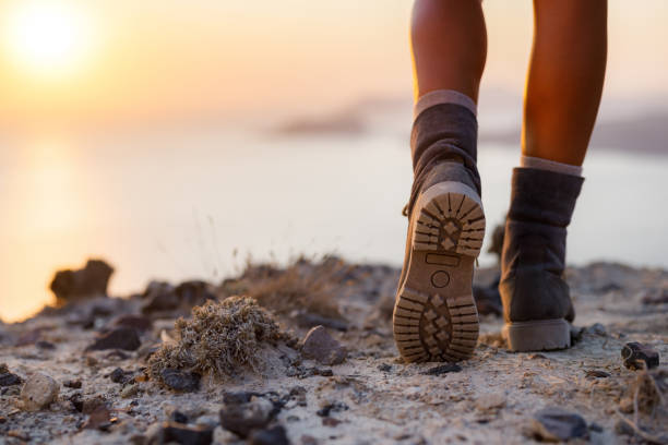 Close up of unrecognizable hiker in hiking boots walking on a hill above the sea at sunset. Copy space.