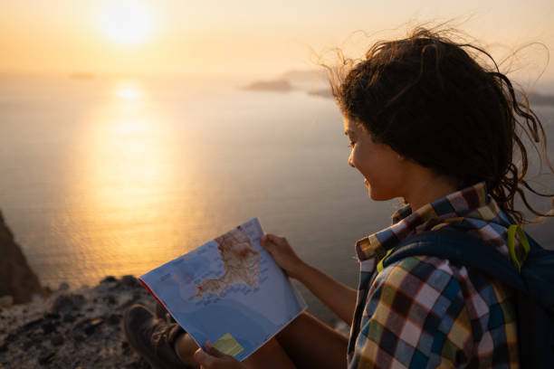istock Happy hiker reading a map on a hill above the sea at sunset. 1354158972