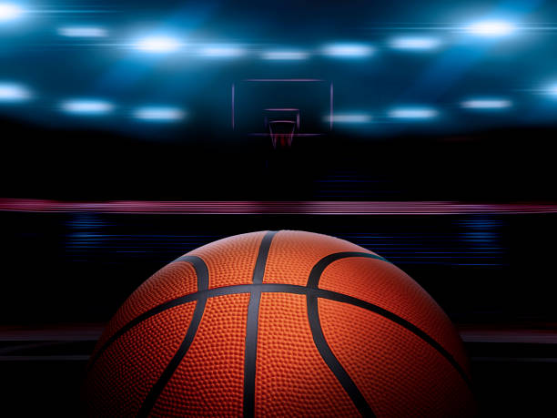 An indoor basketball court with an orange ball on an unmarked wooden floor under illuminated floodlights An indoor basketball court with an orange ball on an unmarked wooden floor under illuminated floodlights basketball stock pictures, royalty-free photos & images