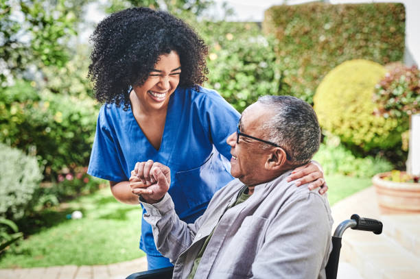 aufnahme einer attraktiven jungen krankenschwester, die draußen steht und ihrem älteren patienten in seinem rollstuhl hilft - senior adult stock-fotos und bilder