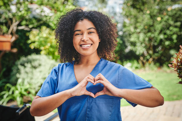 外で一人で立って、ハート型のジェスチャーをする魅力的な若い看護師のショット - i love my job ストックフォトと画像