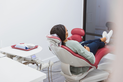 Lying down on the dental chair, the unrecognizable mid adult female patient clasps her hands as she waits for the dentist.