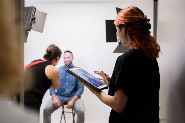 Focus on female assistant adjusting photos as photographer shoots The focus of the photo is on the mid adult female assistant as she adjusts the photos on the digital tablet that the unrecognizable mid adult female photographer shoots of the mid adult male client. pre press stock pictures, royalty-free photos & images