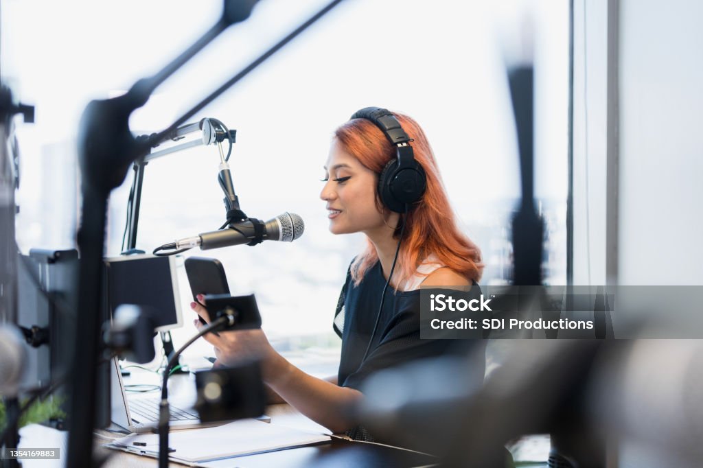 Focus on female podcaster live streaming show The focus of the photo is on the mid adult female podcaster live streaming a show.  She is in a modern studio with state-of-the-art equipment. Podcasting Stock Photo