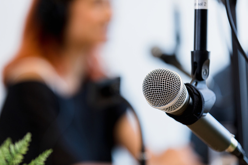 The focus of the photo is on the microphone in the foreground.  The unrecognizable male and female radio show co-hosts sit in background.