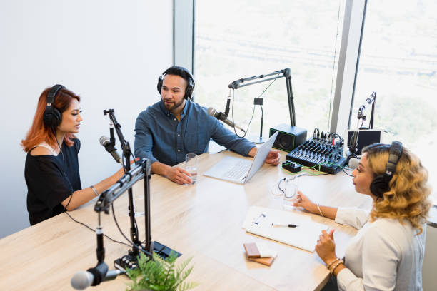 istock Radio show hosts sit across from guest in studio 1354169912