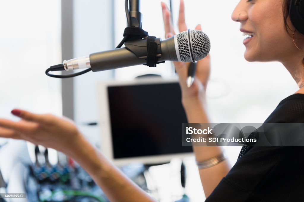 Mid adult woman gestures while recording podcast in studio An unrecognizable mid adult woman gestures as she records a podcast in a studio.  The focus of the photo is on the woman speaking into a microphone. Desktop PC Stock Photo
