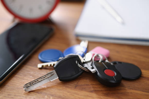 Close-up of bundle of car remote keys and keys from home and buzzer. Smartphone with black screen on wooden table. Access to your property, mockup concept