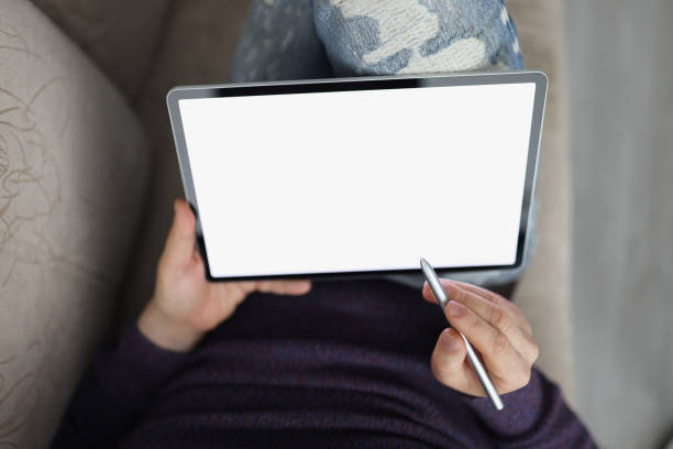 Top view of male hands holding tablet with stylus. Man lying on sofa and surfing internet on modern gadget. Distance or remote work concept. Copy space on empty screen