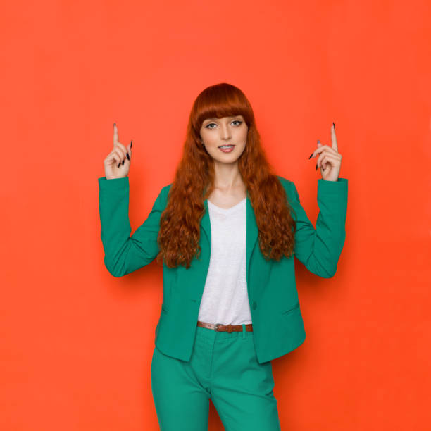Confident young red haired girl in green costume is pointing up stock photo