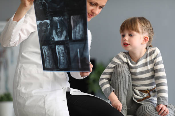 女性医師は小さな女の子に背骨のx線写真を示しています - scoliosis ストックフォトと画像