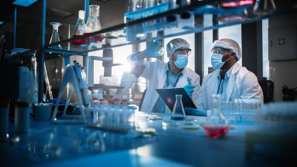 istock Modern Medical Research Laboratory: Two Scientists Wearing Face Masks use Microscope, Analyse Sample in Petri Dish, Discuss Innovative Technology. Advanced Scientific Lab for Medicine, Biotechnology 1354171849