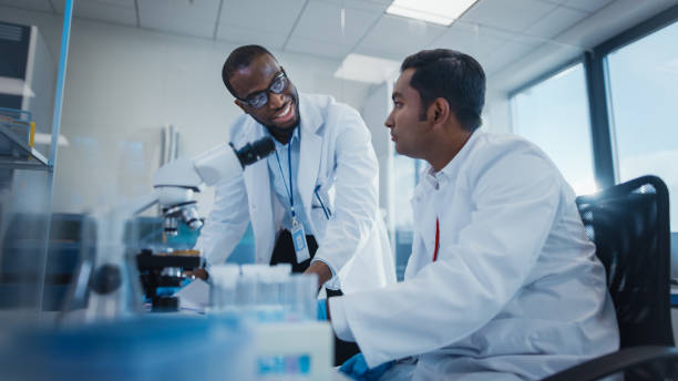 istock Modern Medical Research Laboratory: Two Smiling Male Scientists Working Together Using Microscope, Analysing Samples, Talking. Advanced Scientific Lab for Medicine, Biotechnology. 1354172470