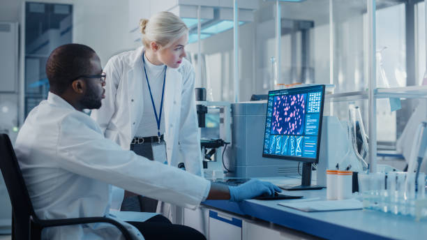 現代医学研究所:2人の科学者がdna遺伝子分析を示すスクリーン付きのコンピュータを使用し、専門家が革新的な技術について議論します。医学・バイオテクノロジー先端科学研究室 - scientist research group of people analyzing ストックフォトと画像