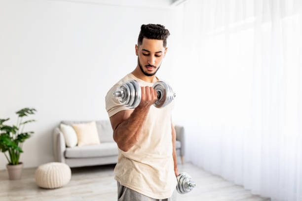 istock Domestic training concept. Strong young Arab man exercising with dumbbells at home 1354172533