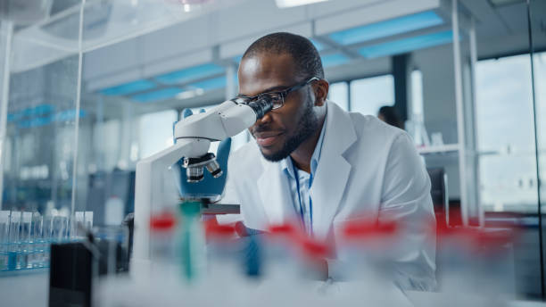 modern medical research laboratory: ritratto di uno scienziato maschio che guarda al microscopio, analizzando campioni. laboratorio scientifico avanzato per lo sviluppo di medicina, biotecnologie, microbiologia - laboratory scientist african ethnicity science foto e immagini stock