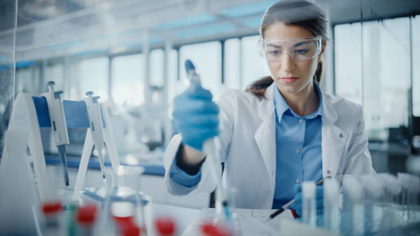 의학 연구 실험실: 시험 분석을 위해 마이크로 파이펫을 사용하여 고글에 있는 아름다운 여성 과학자의 초상화. 의학, 생명 공학, 미생물학 개발을위한 고급 과학 연구소 - 과학 뉴스 사진 이미지