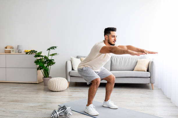 istock Handsome young Arab man doing squats, working out at home, full length 1354172793