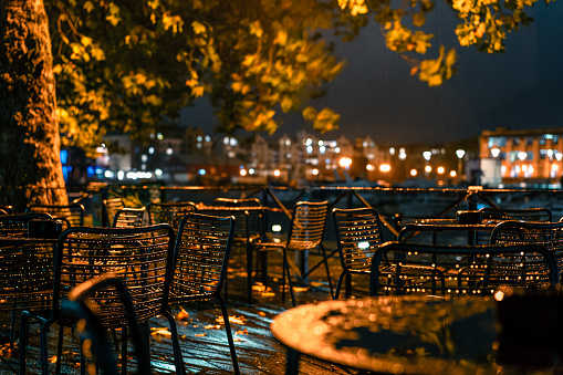 City cafe terrace near the river in the rainy autumn evening in the lantern light. Raindrops on outdoor metal furniture. Urban fall concept.Selective focus