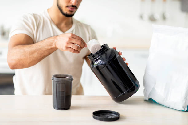Unrecognizable young sporty guy making protein shake at table in kitchen, closeup stock photo