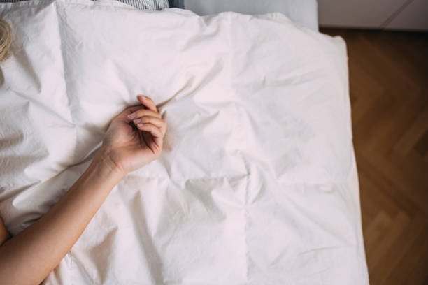 Top View Of Woman Wearing Pajamas Lying In Bed, Holding White Pillow Over Her Face. Unrecognizable Lazy Lady Feeling Tired And Unmotivated In The Morning, Dont Want To Get Up