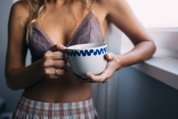 une femme en pyjama tenant une tasse de café - the human body photos et images de collection