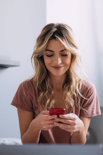 a blonde woman texting and smiling - t shirt shirt pink blank imagens e fotografias de stock