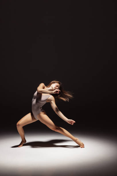 istock Dynamic portrait of young flexible contemp dancer dancing isolated on dark studio background in spotlight. Art, beauty, inspiration concept. 1354173780