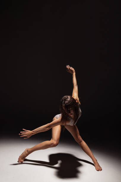 istock Dynamic portrait of young flexible contemp dancer dancing isolated on dark studio background in spotlight. Art, beauty, inspiration concept. 1354173793