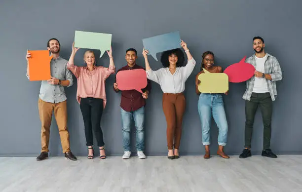 Photo of Full length portrait of a young and diverse group of businesspeople holding up blank placards in the shape of speech bubbles against a grey background in studio