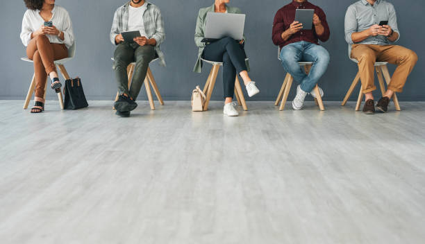 istock Cropped shot of an unrecognizable group of businesspeople using their wireless devices while seating in line for interviews against a grey background in studio 1354173958
