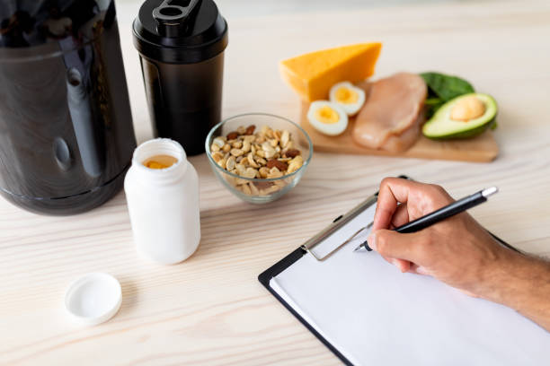 closeup of young bodybuilder writing meal plan on clipboard with mockup, eating healthy foods, using protein shakes - body building milk shake protein drink drink imagens e fotografias de stock