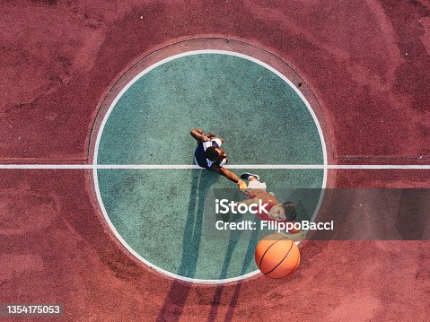 istock Two friends are jumping to take a basketball ball on the center field 1354175053